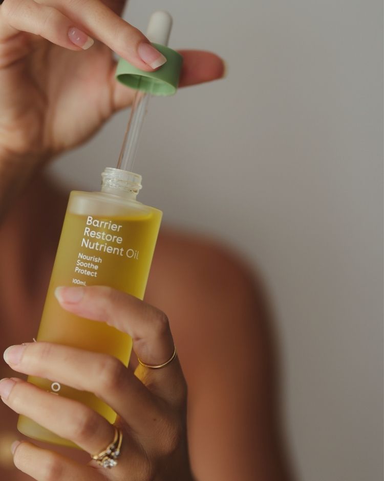 Hand holding a bottle of Barrier Restore Nutrient Oil with a dropper against a neutral background