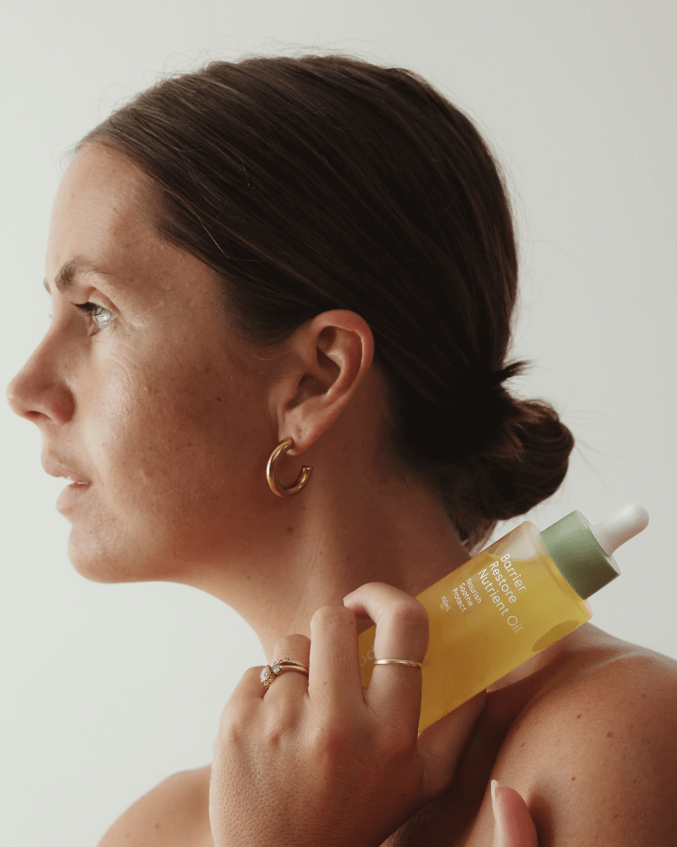 Woman applying a yellow skincare product to her neck with a neutral background