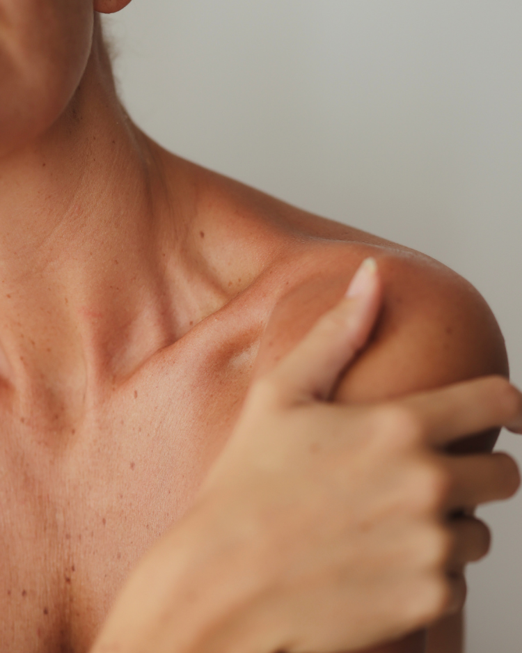 Hand pointing to a shoulder with visible skin texture on a plain background