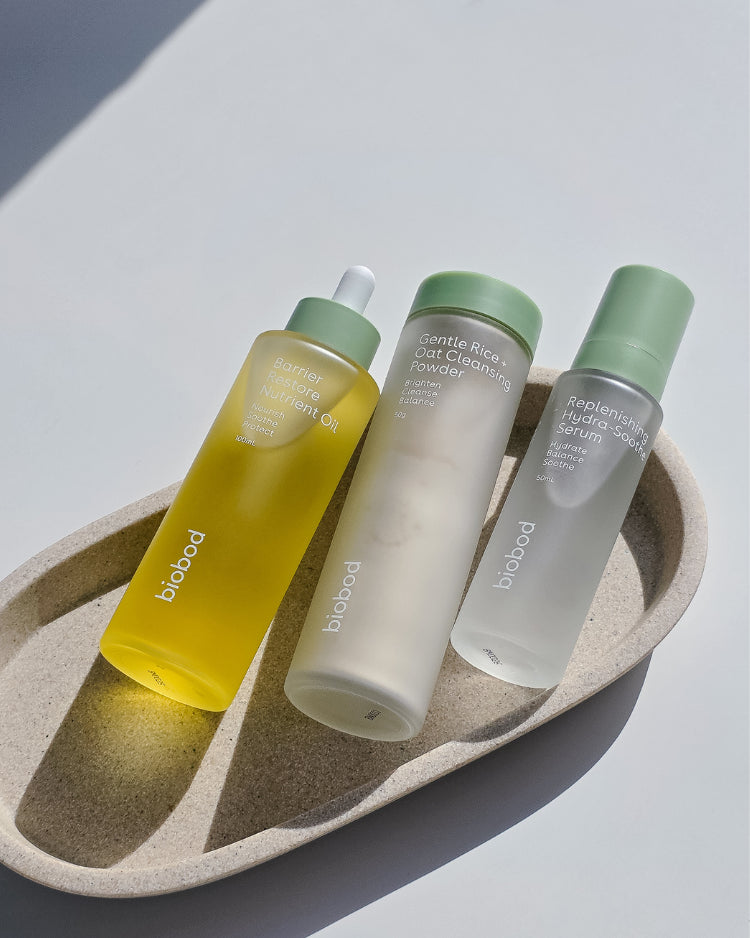 Three skincare bottles on a textured stone tray with a neutral background